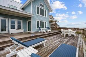 Une maison bleue avec une terrasse en bois, un espace salon extérieur et une vue sur l’océan.