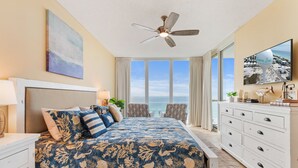 A bedroom with a large bed, a ceiling fan, a TV, and a view of the ocean. - Gulf Front Resort w/Pools. 2 chairs/umbrella included for your stay! (Navarre)
