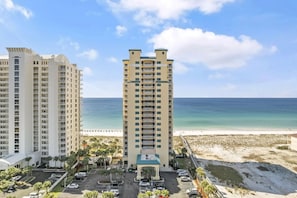 A high-rise hotel with a central courtyard, a parking lot, and a beach view.