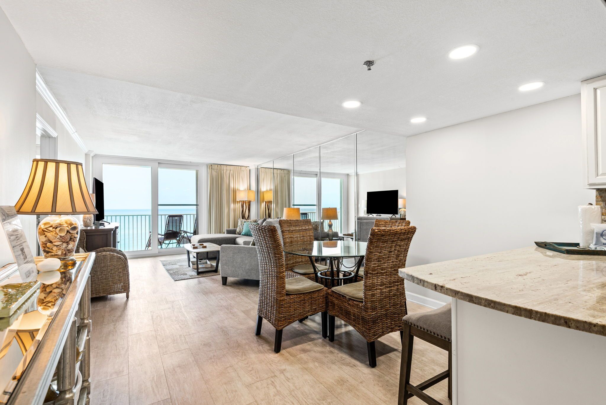 A modern hotel room with a dining area, a living room with a sofa and chairs, a kitchen area, and large windows offering a view.