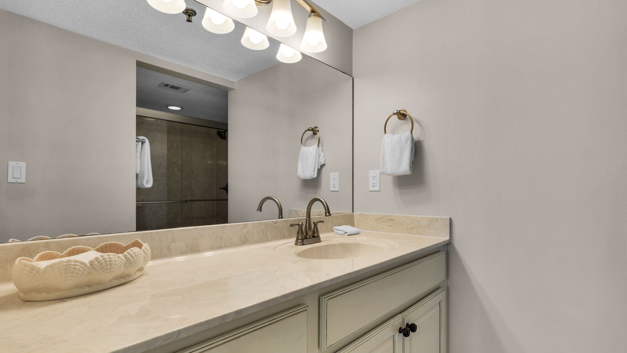 A bathroom with a large mirror, a sink with a towel ring, and a towel rack.