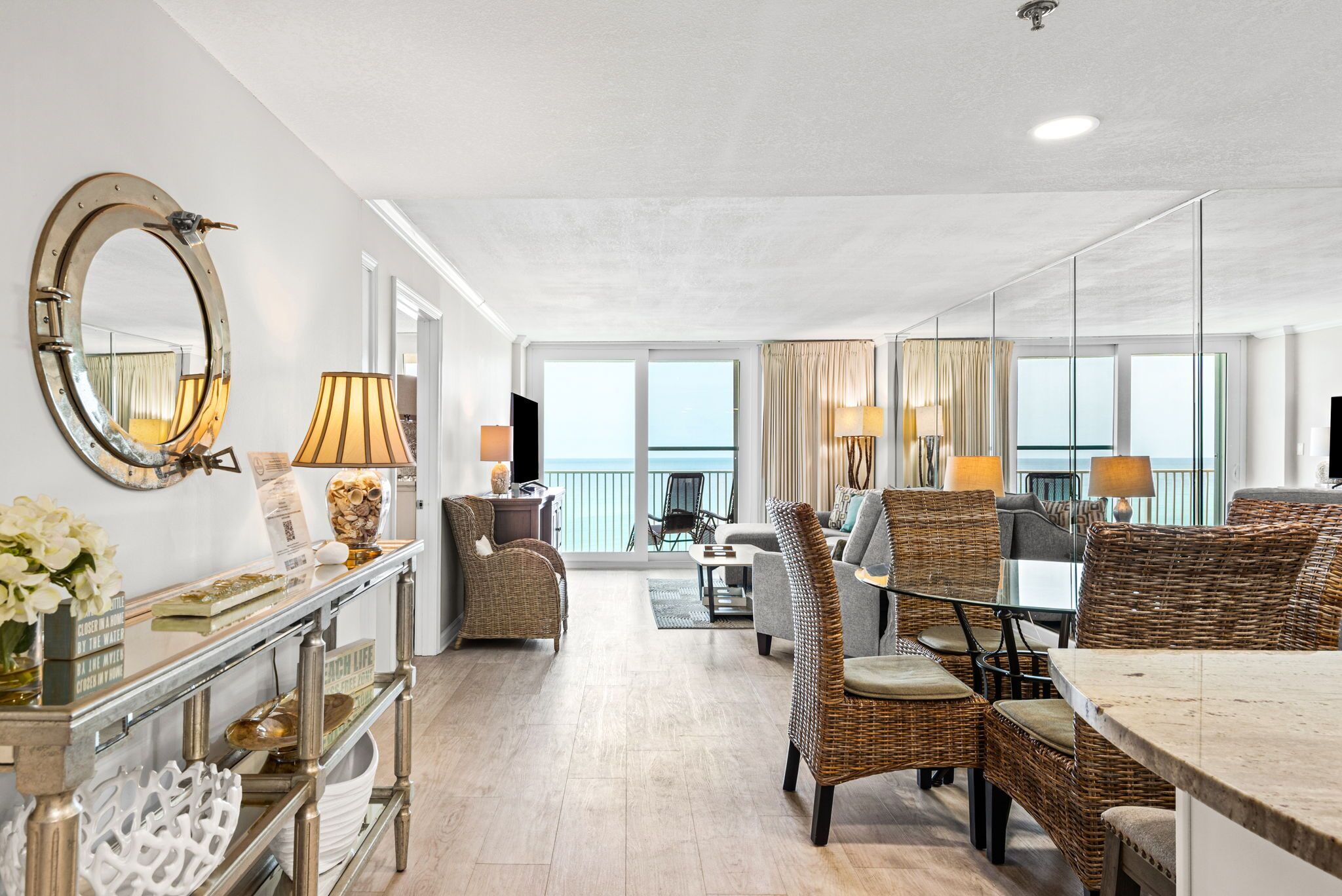 A spacious living area with a large mirror, wicker furniture, and a view to the outside.