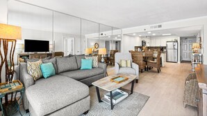 Een moderne woonkamer met een hoekbank, een salontafel en een eethoek met rieten meubels.