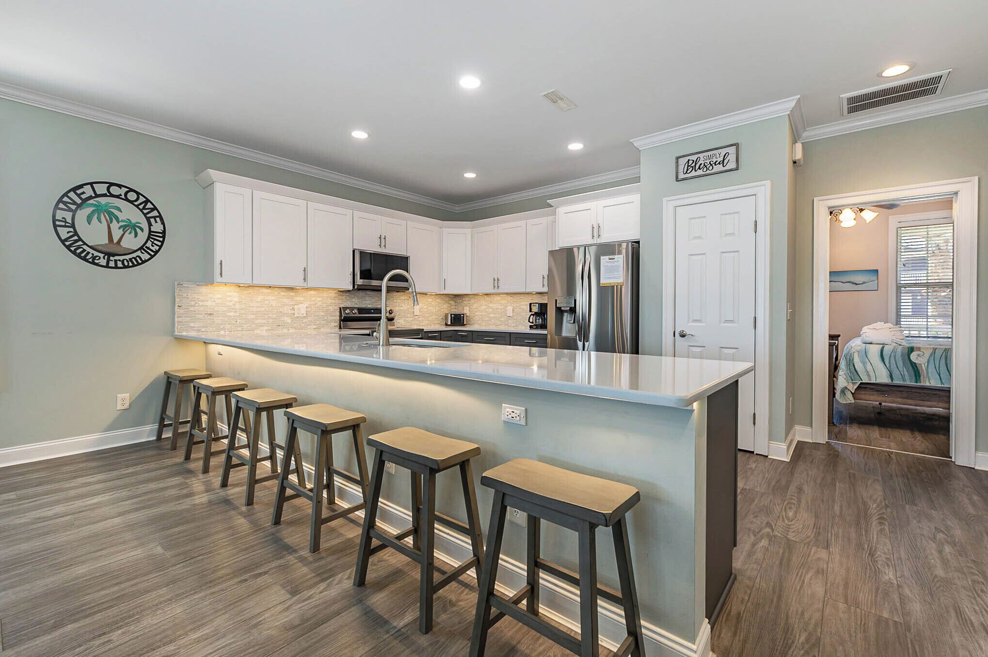 A modern kitchen with a central island, bar stools, and a welcome sign.