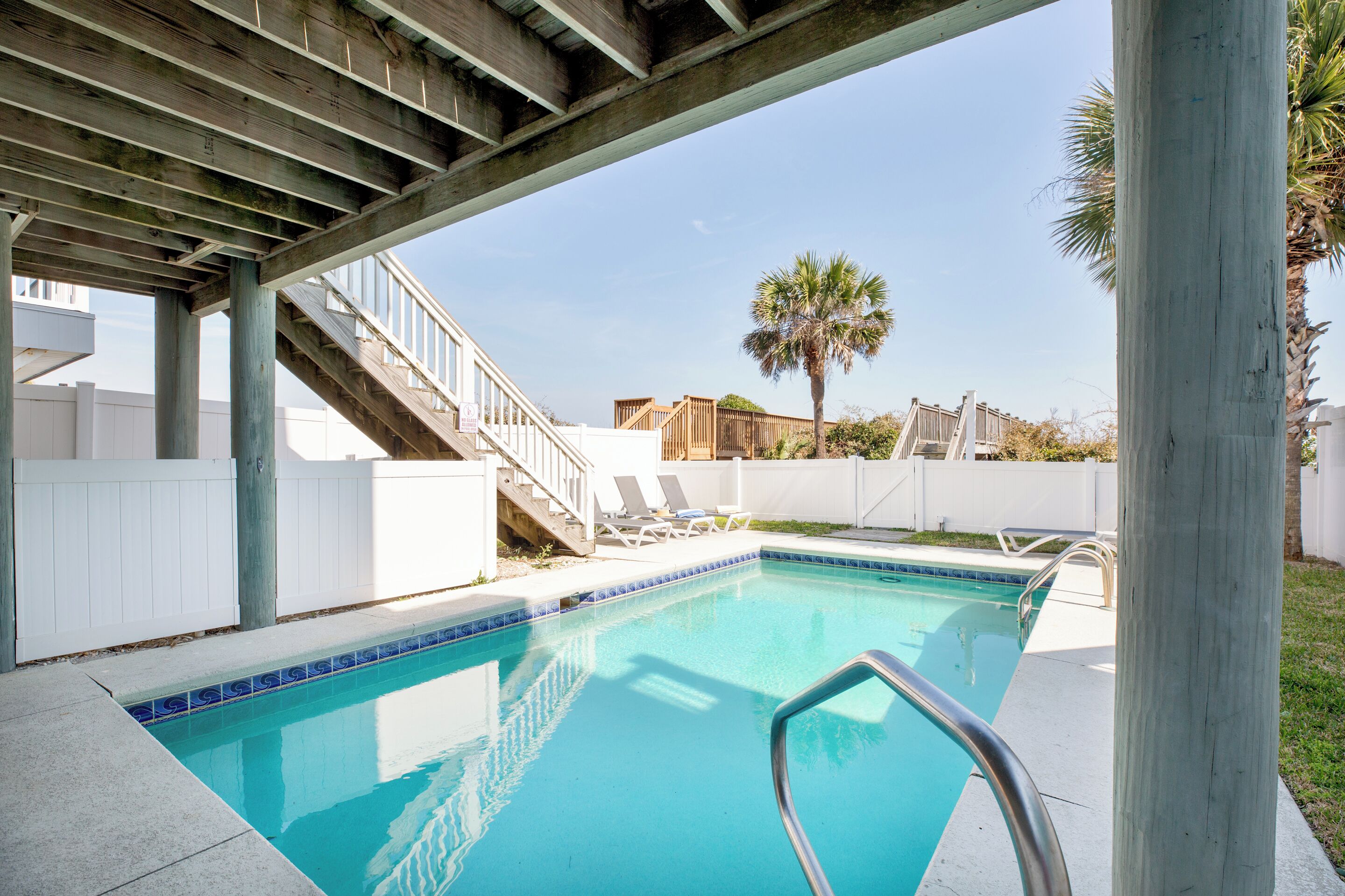 A swimming pool with a wooden deck, a staircase, and a palm tree in the background.