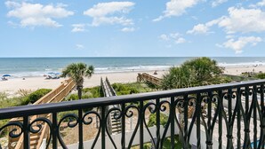 A beach view from a balcony with a railing, palm trees, and a wooden walkway leading to the beach. - A Wave From It All: Oceanfront & Pool (Surfside Beach)
