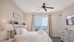 A bedroom with a bed, bedside lamps, a ceiling fan, a window with curtains, a dresser, and a TV on the wall. - A Wave From It All: Oceanfront & Pool (Surfside Beach)