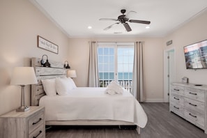 Un dormitorio con cama, lámparas de noche, ventilador de techo, ventana con cortinas, cómoda y televisor en la pared.