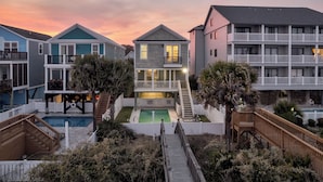 A beachfront property with a pool, a staircase leading to a balcony, and a wooden deck. - A Wave From It All: Oceanfront & Pool (Surfside Beach)
