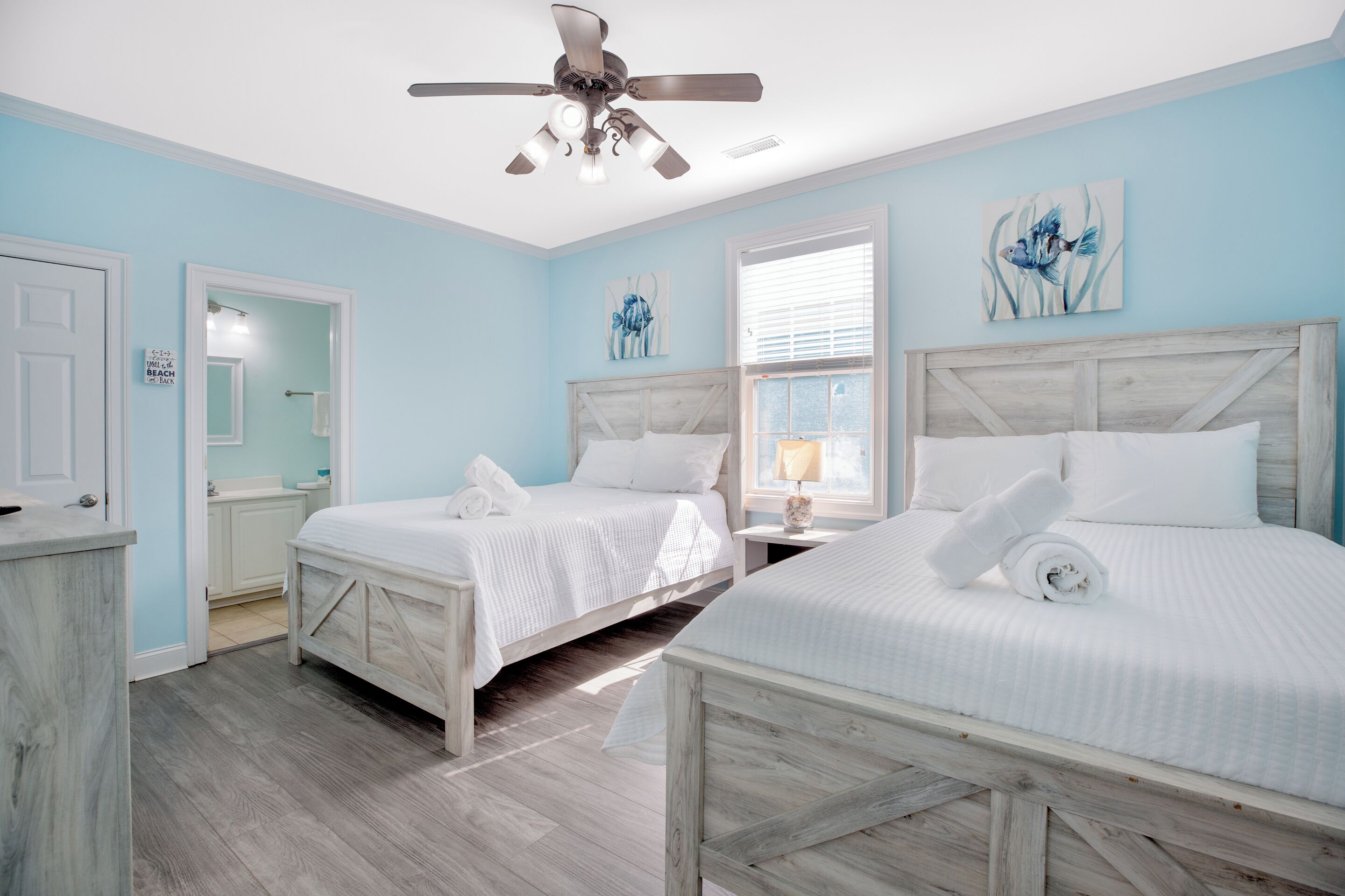 A bedroom with two beds, a ceiling fan, artwork, and a window.