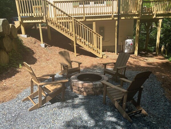 A wooden deck with a stone fire pit and four Adirondack chairs.