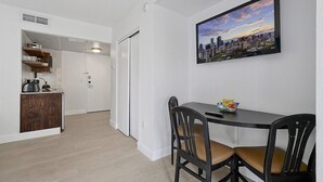 Un comedor con una mesa y sillas, un cuadro de un paisaje urbano en la pared y una zona de cocina con armarios y una encimera.