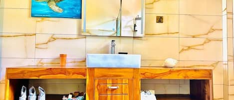 A bathroom with a wooden vanity, a sink, and a mirror. There is a painting of a sea turtle on the wall.