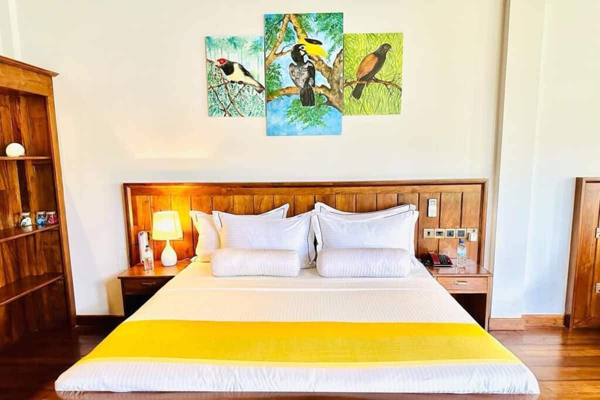 A hotel room with a wooden bed, white bedding, a yellow throw, and a wall with three bird paintings.
