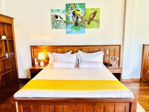 A hotel room with a wooden bed, white bedding, a yellow throw, and a wall with three bird paintings. - Lagoon gate Tangalle Resort  (Rekawa)