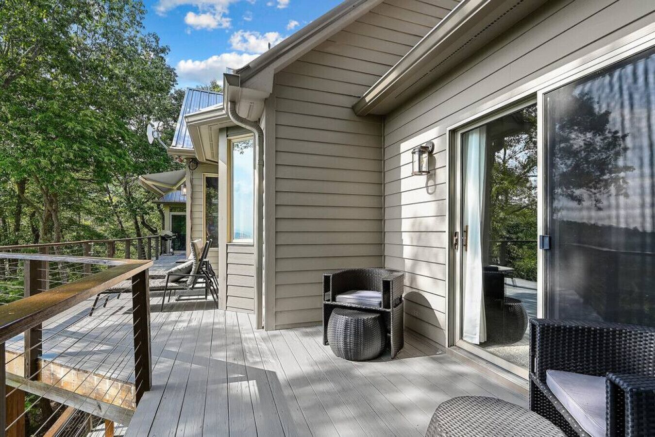 A deck with outdoor furniture, a glass door leading to a covered area, and a view of trees.