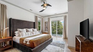 Un dormitorio moderno con una cama grande, televisor y un balcón con vistas a zonas verdes.