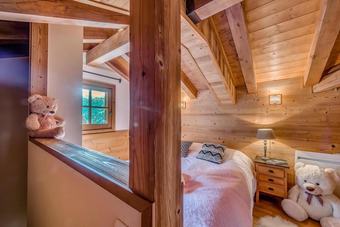 Quarto de cabana aconchegante com teto de madeira, uma cama com edredom branco, mesa de cabeceira, abajur e dois ursinhos de pelúcia.
