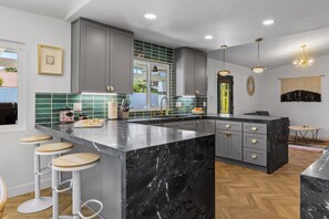 A modern kitchen with grey cabinets, a black marble island, and wooden stools. - Out Of Office – Sophisticated Desert Retreat (Palm Springs)