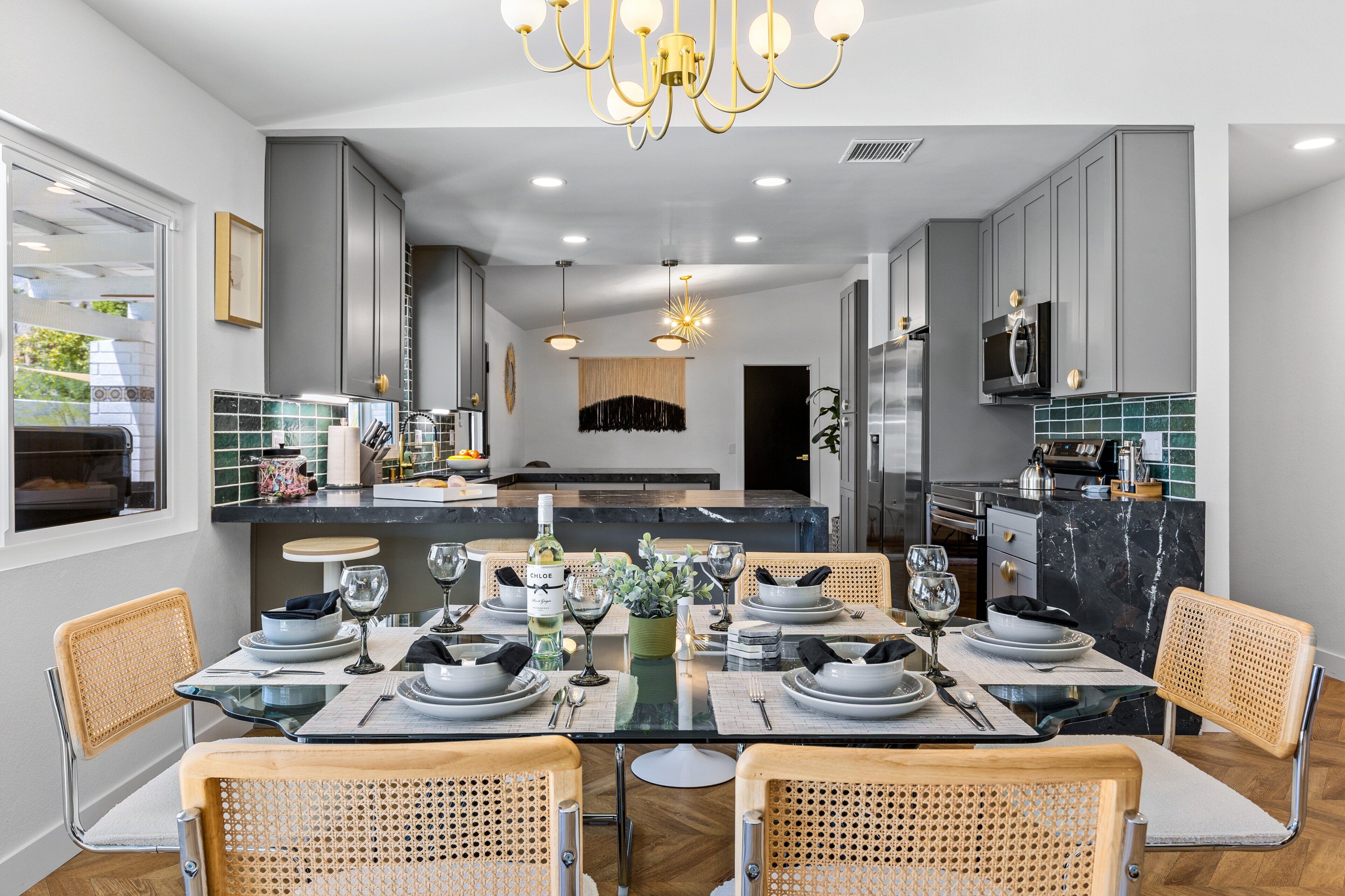A modern kitchen with grey cabinets, a black marble island, and a dining area with a glass table and wicker chairs.