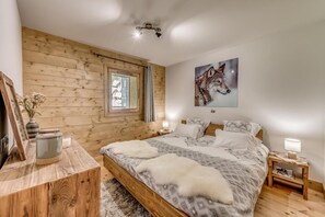 Ein gemütliches Schlafzimmer mit Holzwand, einem großen Bett mit gemusterten Betttextilien, einem gerahmten Bild eines Wolfs und einem Nachttisch mit Lampe.