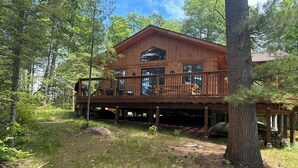 A wooden cabin with a deck, surrounded by trees.