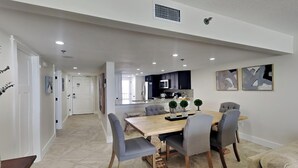 Un espace repas moderne avec une table en bois et des chaises grises, une cuisine en arrière-plan et un couloir menant à une autre pièce.