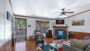 A living room with hardwood flooring, a ceiling fan, a fireplace, a blue armchair, and a coffee table with a star-patterned rug.