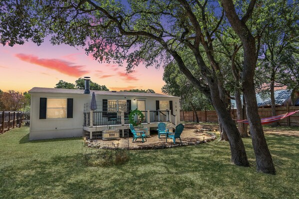A small house with a covered patio, two blue chairs, and a hammock.