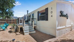 A single-story mobile home with a number '104' on the side, a covered porch, and a small patio area with outdoor furniture.