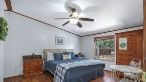 A bedroom with a bed, wooden dresser, nightstands, a ceiling fan, and a window with blinds.