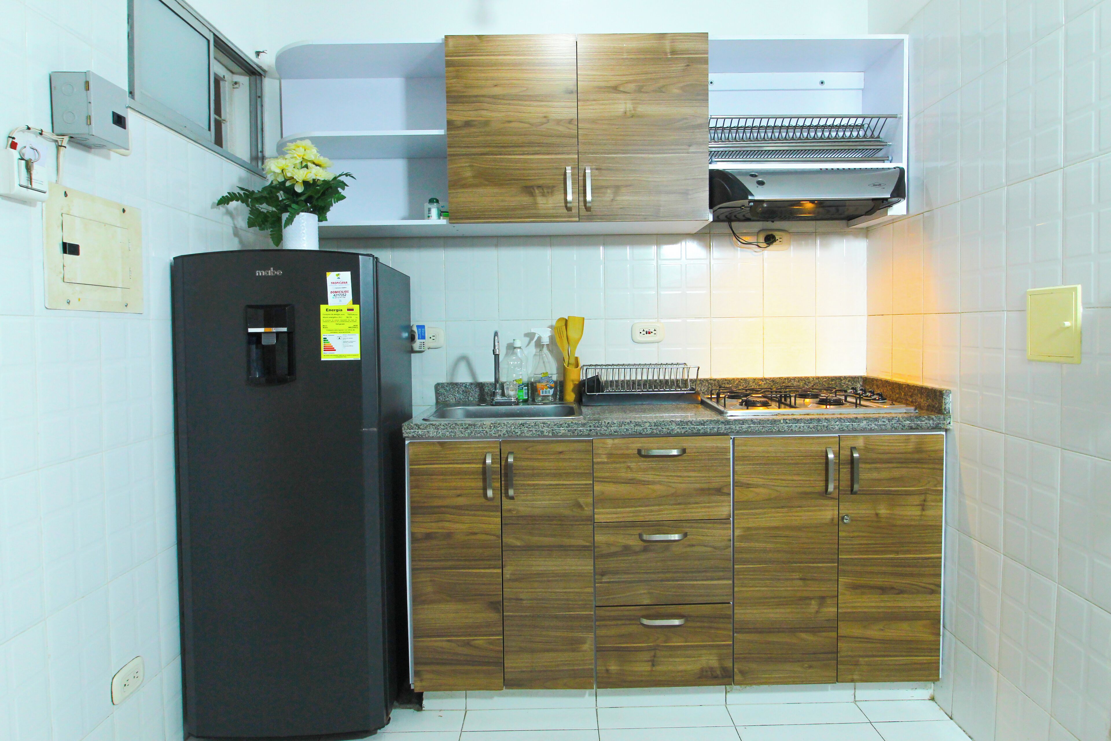 A kitchen with a black refrigerator, wooden cabinets, a stainless steel range hood, and a white tiled backsplash.