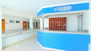 A reception area with a blue counter, a wooden panel display, and a sign that reads "RECEPCION".