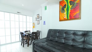 A modern living room with a black leather sofa, a dining table with chairs, and a large window.