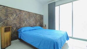 A bedroom with a bed, a nightstand, a wooden cabinet, and a large window.