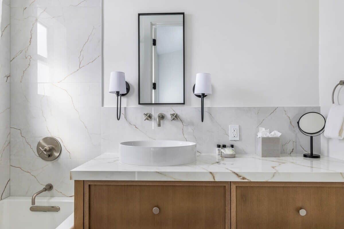 A modern bathroom with a marble vanity, a round sink, two wall-mounted lamps, a mirror, and a towel rack.