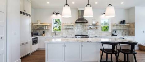 A modern kitchen with white cabinetry, a large island, pendant lighting, and a view of greenery outside.