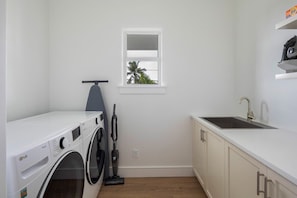 A laundry area with a washing machine, a vacuum cleaner, a window, and a sink.