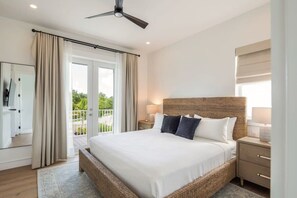 Ein geräumiges Schlafzimmer mit einem großen Bett, einem Deckenventilator, einem Balkon mit Vorhängen und Blick auf Grün.