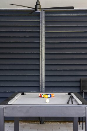 A pool table with balls and cues, set against a dark wooden backdrop.