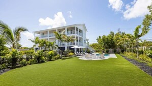 Une maison à deux étages avec une piscine, entourée d’une pelouse bien entretenue et de palmiers.