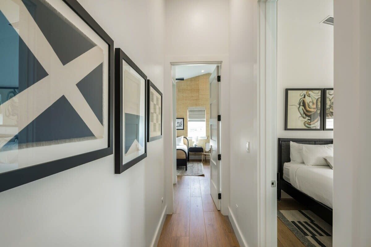 A hallway with framed artwork, a bed, and a view into a bedroom.