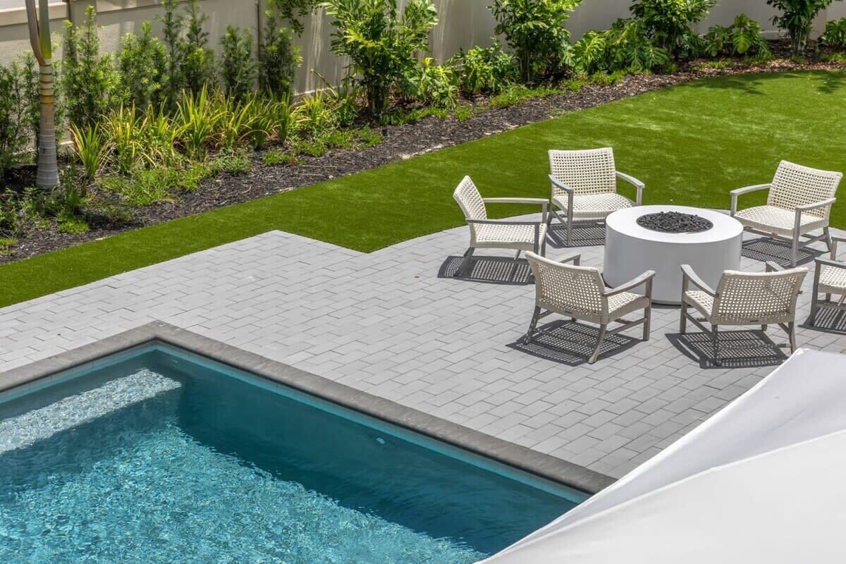 Une piscine avec un espace patio, entourée d’une pelouse bien entretenue et de diverses plantes.