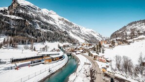 Un pueblo cubierto de nieve en la montaña, con un río, edificios de madera y una estación de tren.