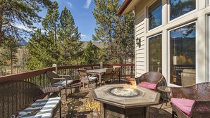Une terrasse extérieure aménagée avec des meubles en osier, un foyer et une vue sur les arbres et les montagnes.