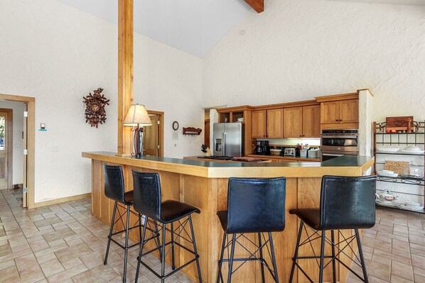 A kitchen with a central island, wooden cabinets, a refrigerator, an oven, and bar stools.