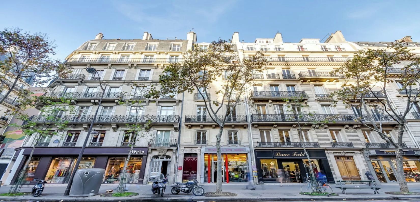 Un edificio de varios pisos con locales comerciales en la planta baja, incluyendo una tienda de ropa y una zapatería.