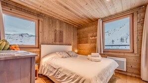 Un dormitorio acogedor en una cabaña de madera con una cama grande, una mesita de noche y vistas a un paisaje montañoso nevado.