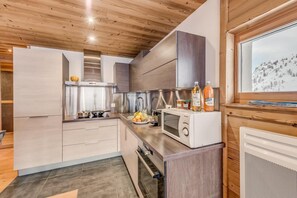 A modern kitchen with wooden cabinets, a microwave, and a window with a snowy view. - 20m from resort center, 6th floor, view mountain, balcony, tv, ski locker, 55m², Tignes (Tignes)