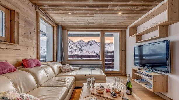 Un salón acogedor con un sofá de cuero, una mesa de centro de madera con aperitivos, un televisor y vistas a la montaña.
